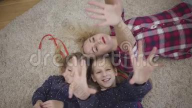 镜头接近年轻的白种人母亲躺在柔软的地毯上，双手举起。 开朗的家庭